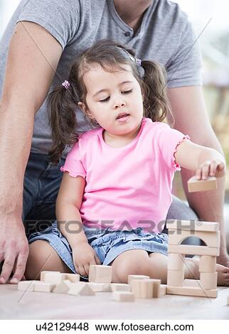 Stock Photo - Little girl playing with wooden blocks against father in house. Fotosearch