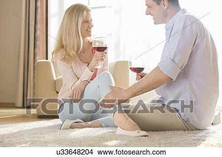 Picture - Loving couple looking at each other while drinking red wine at home. Fotosearch