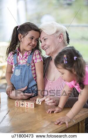 Stock Image - Loving grandmother teaching calculation to granddaughters at table in house. Fotosearch