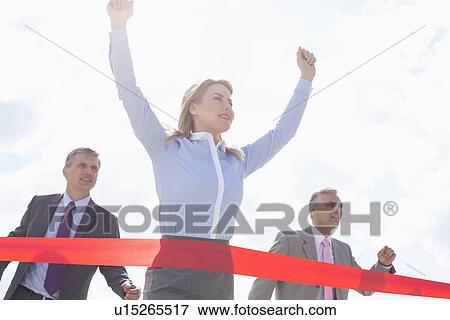 Low angle view of businesswoman crossing finishing line with colleagues in background View Large Photo Image Stock Photo - Low angle view of businesswoman crossing finishing line with colleagues in background. Fotosearch