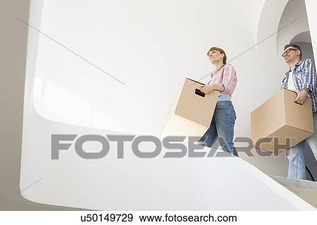 Low angle view of couple with boxes moving into new house View Large Photo Image Stock Photo - Low angle view of couple with boxes moving into new house. Fotosearch