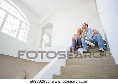 Stock Photography - Low angle view of couple with painting tools sitting on steps in new house. Fotosearch