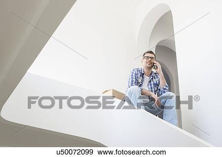 Low angle view of man using cell phone in new home View Large Photo Image Stock Photo - Low angle view of man using cell phone in new home. Fotosearch