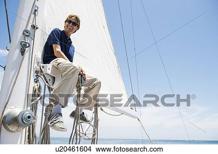 Picture - Low angle view of smiling man sitting on yacht boom. Fotosearch