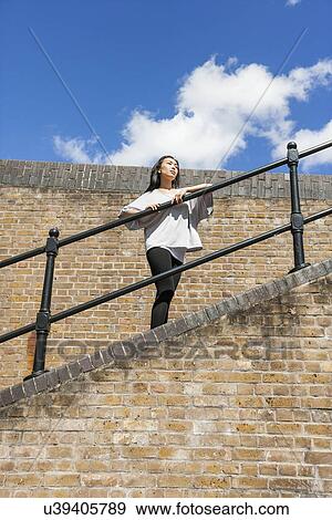 Low angle view of young woman looking away while leaning on railing against cloudy sky View Large Photo Image Stock Photo - Low angle view of young woman looking away while leaning on railing against cloudy sky. Fotosearch