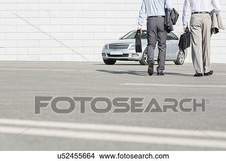 Low section of businessmen carrying briefcases while walking towards car on street View Large Photo Image Picture - Low section of businessmen carrying briefcases while walking towards car on street. Fotosearch