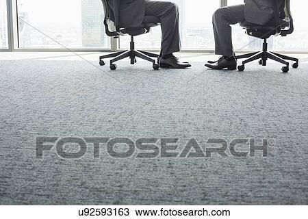 Stock Image - Low section of businessmen sitting on office chairs. Fotosearch