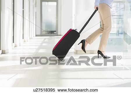 Stock Photography - Low section of businesswoman with luggage exiting airport. Fotosearch
