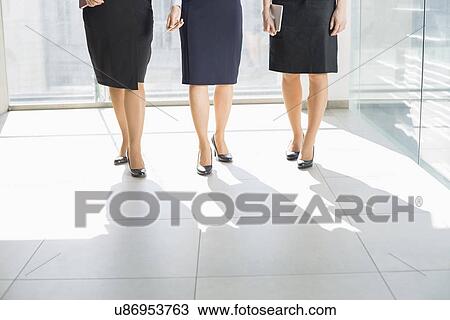 Stock Image - Low section of businesswomen standing on tiled floor in office. Fotosearch