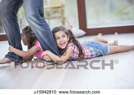 Stock Image - Low section of father dragging girls on hardwood floor. Fotosearch