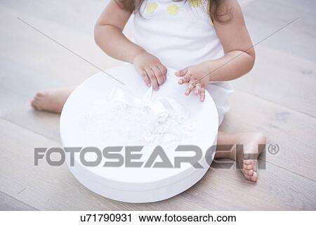 Stock Image - Low section of little girl opening gift box on floor at home. Fotosearch