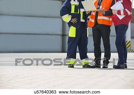 Stock Image - Low section of workers discussing in shipping yard. Fotosearch