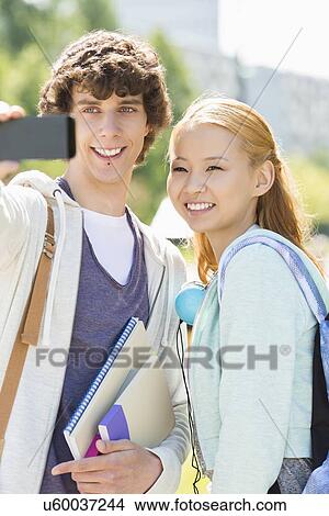 Picture - Male and female friends taking selfie with smart phone at college campus. Fotosearch