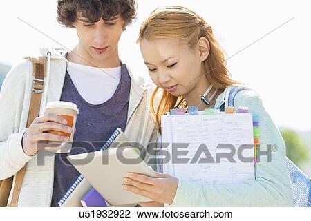 Stock Image - Male and female friends using digital tablet at college campus. Fotosearch