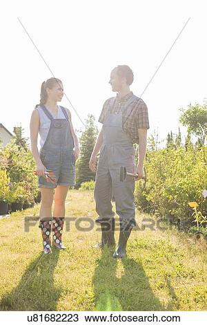 Stock Image - Male and female gardeners conversing at plant nursery. Fotosearch