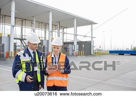 Stock Photograph - Male and female workers discussing over clipboard in shipping yard. Fotosearch
