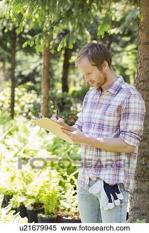 Stock Photography - Male supervisor writing on clipboard at plant nursery. Fotosearch