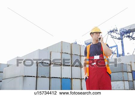 Stock Image - Male worker using walkie-talkie in shipping yard. Fotosearch