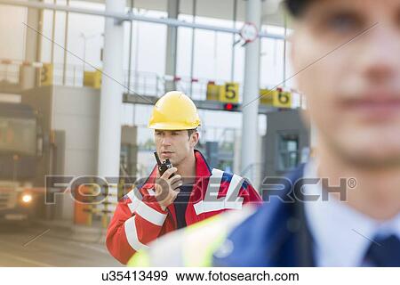 Male worker using walkie-talkie with colleague in foreground at shipyard View Large Photo Image Stock Photo - Male worker using walkie-talkie with colleague in foreground at shipyard. Fotosearch