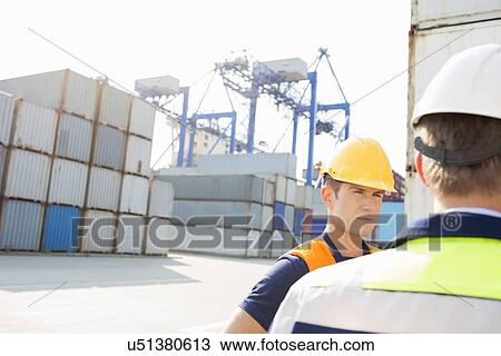 Stock Image - Male workers standing in shipping yard. Fotosearch