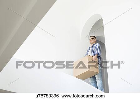 Stock Photograph - Man carrying cardboard box in new home. Fotosearch