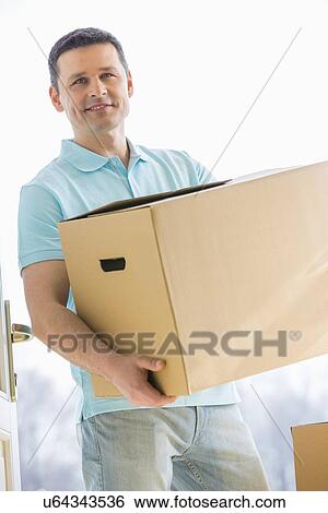 Stock Photograph - Man looking away while carrying cardboard box while entering new house. Fotosearch