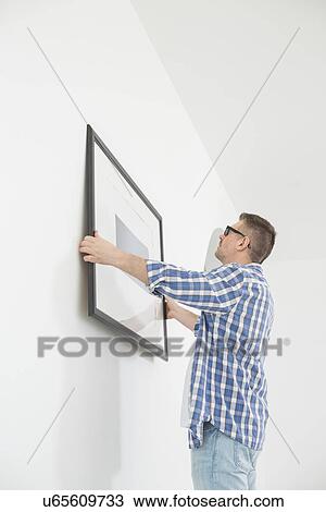 Stock Image - Man positioning picture frame on wall. Fotosearch