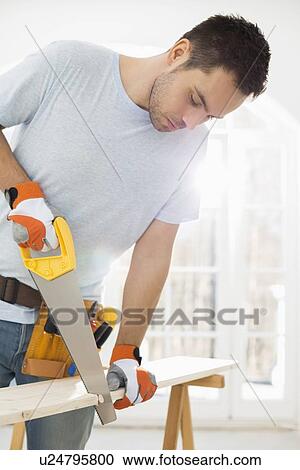 Stock Image - Man sawing wood in new house. Fotosearch