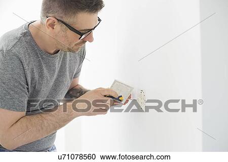 Stock Image - Man working on electrical outlet. Fotosearch