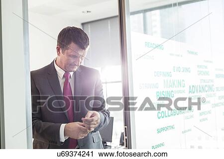 Stock Image - Mature businessman buttoning sleeve in office. Fotosearch