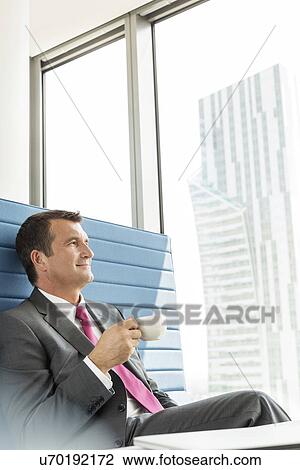 Stock Image - Mature businessman having coffee in office. Fotosearch