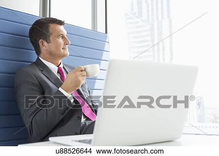 Mature businessman taking coffee break in office View Large Photo Image Picture - Mature businessman taking coffee break in office. Fotosearch