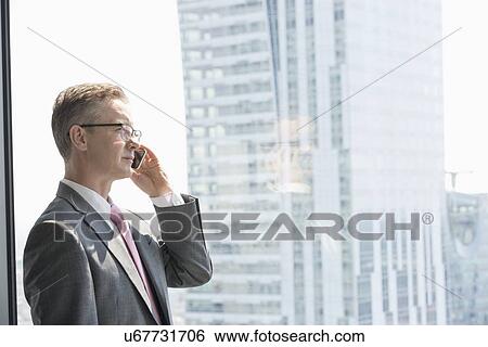 Stock Photograph - Mature businessman talking on cell phone by window. Fotosearch