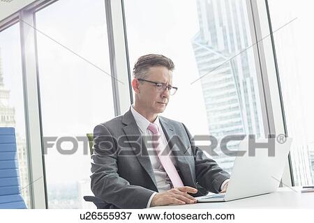 Stock Photo - Mature businessman using laptop in office. Fotosearch