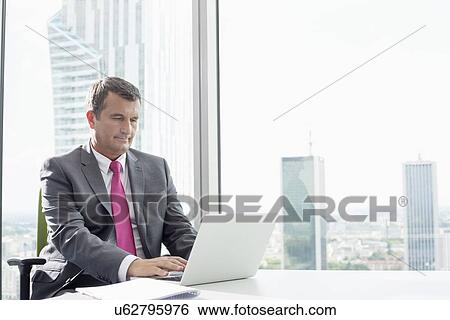 Stock Photograph - Mature businessman using laptop in office. Fotosearch