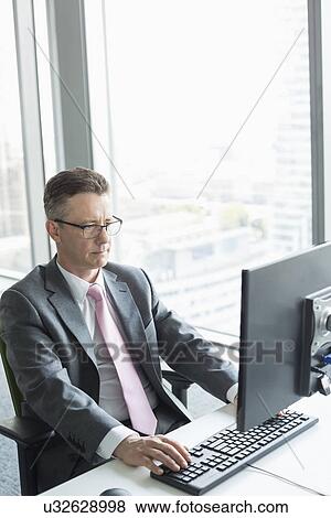 Mature businessman working on computer in office View Large Photo Image Stock Photo - Mature businessman working on computer in office. Fotosearch