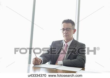 Mature businessman writing on book at table in office View Large Photo Image Stock Image - Mature businessman writing on book at table in office. Fotosearch