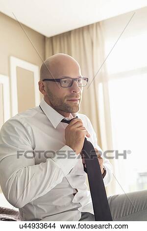 Picture - Mid adult businessman adjusting necktie at home. Fotosearch