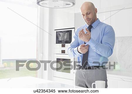Stock Photography - Mid adult businessman buttoning sleeve at home. Fotosearch