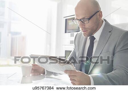 Mid adult businessman having coffee while reading newspaper at home View Large Photo Image Picture - Mid adult businessman having coffee while reading newspaper at home. Fotosearch