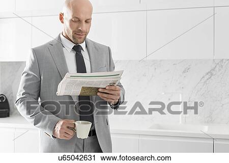 Mid adult businessman having coffee while reading newspaper in kitchen View Large Photo Image Stock Image - Mid adult businessman having coffee while reading newspaper in kitchen. Fotosearch