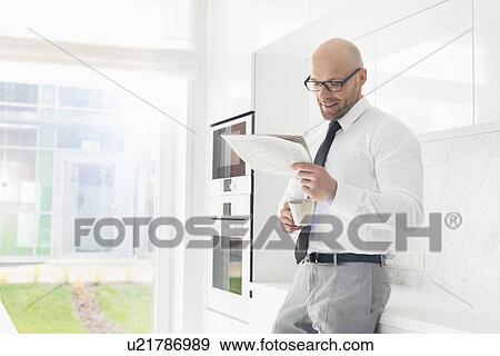 Mid adult businessman having coffee while reading newspaper at home View Large Photo Image Stock Photo - Mid adult businessman having coffee while reading newspaper at home. Fotosearch