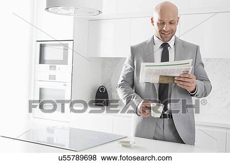 Mid adult businessman having coffee while reading newspaper in kitchen View Large Photo Image Stock Photo - Mid adult businessman having coffee while reading newspaper in kitchen. Fotosearch