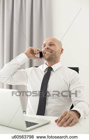 Stock Photo - Mid adult businessman on call in home office. Fotosearch