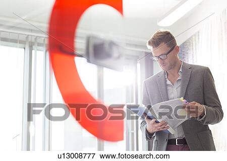 Stock Photo - Mid-adult businessman reading file in creative office. Fotosearch
