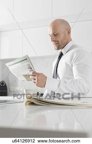Mid adult businessman reading newspaper at kitchen counter View Large Photo Image Stock Image - Mid adult businessman reading newspaper at kitchen counter. Fotosearch