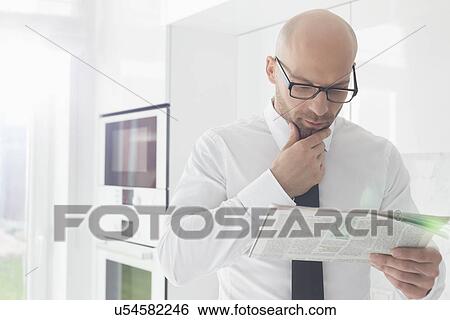 Mid adult businessman reading newspaper at home View Large Photo Image Stock Photograph - Mid adult businessman reading newspaper at home. Fotosearch