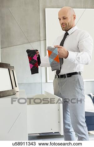 Stock Image - Mid adult businessman selecting socks at home. Fotosearch