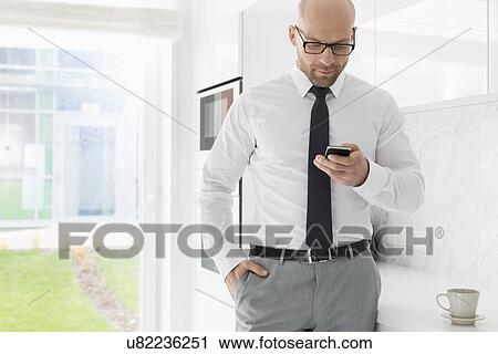 Mid adult businessman text messaging through smart phone at home View Large Photo Image Stock Image - Mid adult businessman text messaging through smart phone at home. Fotosearch