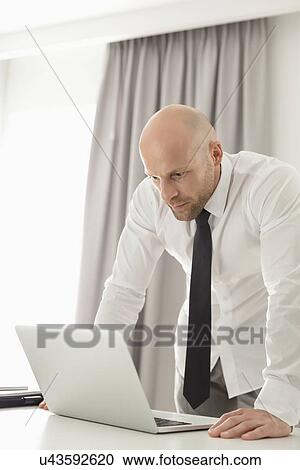 Mid adult businessman using laptop at table in home office View Large Photo Image Stock Image - Mid adult businessman using laptop at table in home office. Fotosearch